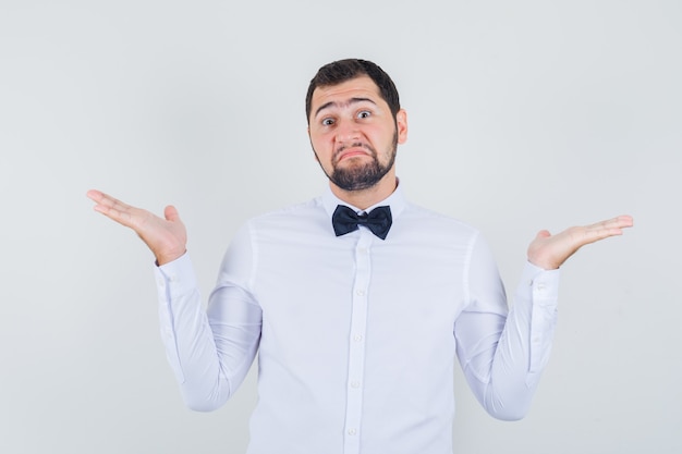 Jeune homme en chemise blanche montrant un geste impuissant et à la confusion, vue de face.