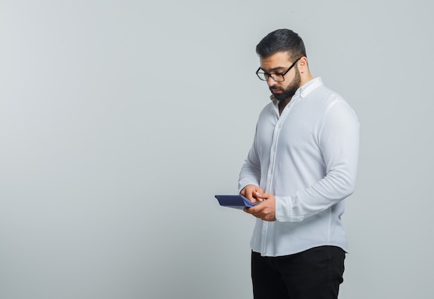 Jeune homme en chemise blanche, pantalon à l'aide de la calculatrice et à occupé