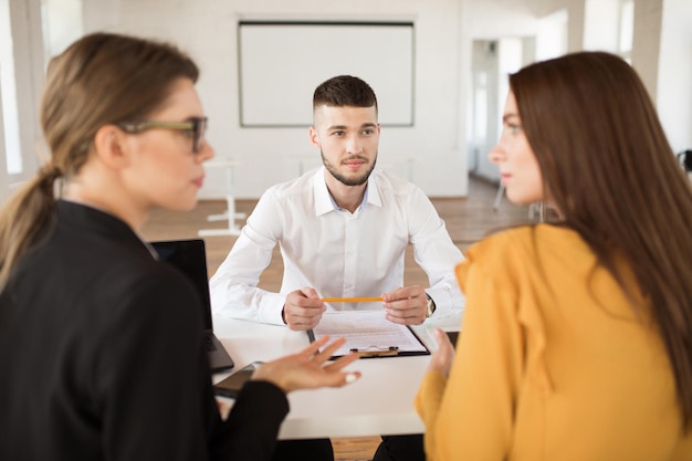 Photo gratuite jeune homme en chemise blanche regardant rêveusement les employeurs tout en passant du temps dans un bureau moderne candidat masculin attendant les résultats de l'entretien d'embauche