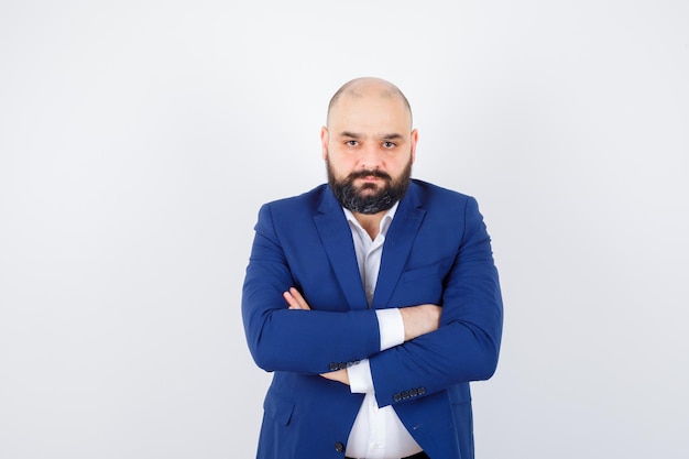 Jeune homme en chemise blanche, veste debout avec les bras croisés et l'air sérieux, vue de face.