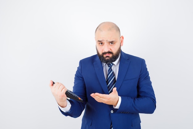 Jeune homme en chemise blanche, veste montrant la calculatrice et hésitant, vue de face.