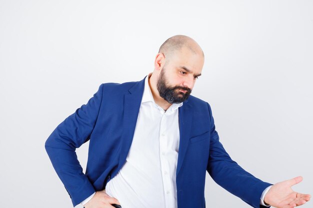 Jeune homme en chemise blanche, veste montrant quelque chose ci-dessous et pensif, vue de face.