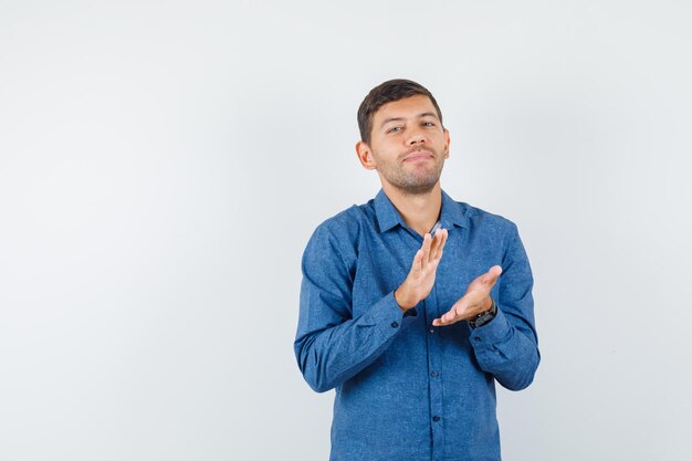 Jeune homme en chemise bleue applaudissant après une excellente présentation et l'air ravi, vue de face.