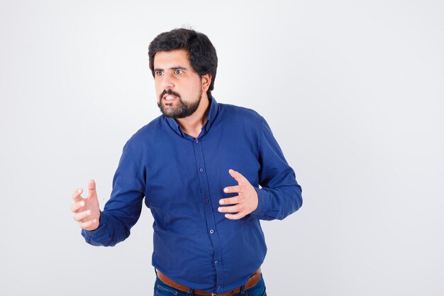 Jeune homme en chemise bleue gardant les mains de manière agressive et regardant en colère, vue de face.