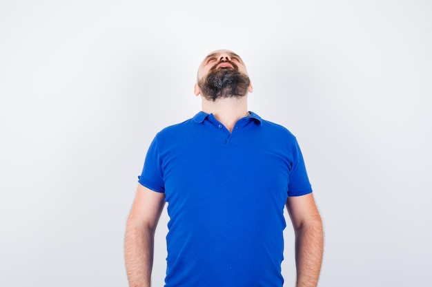 Jeune homme en chemise bleue levant et regardant concentré, vue de face.