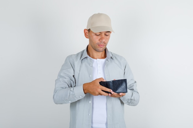 Jeune homme en chemise avec capuchon à la recherche de portefeuille ouvert et à la prudence