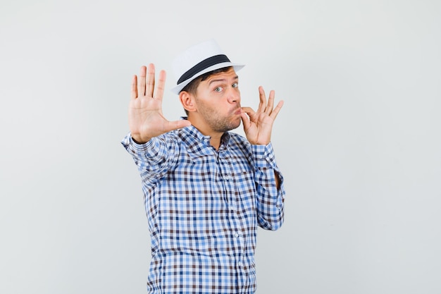 Jeune homme en chemise à carreaux, chapeau montrant la fermeture éclair et le geste d'arrêt
