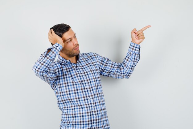 Jeune homme en chemise à carreaux posant tout en pointant vers l'extérieur et à la recherche concentrée