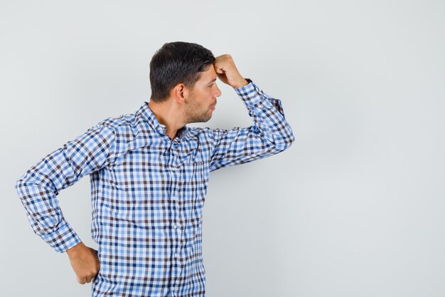 Jeune homme en chemise à carreaux posant tout en regardant de côté et à l'élégant