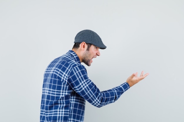 Jeune homme en chemise, casquette levant la main en criant et en regardant en colère.