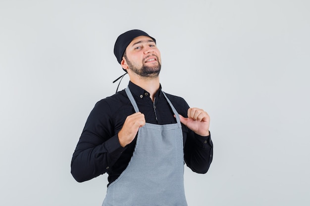 Jeune homme en chemise debout avec les mains touchant le tablier et l'air confiant, vue de face.