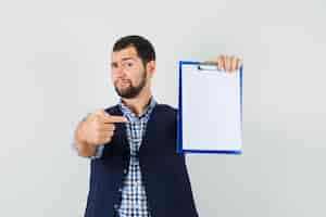 Photo gratuite jeune homme en chemise, gilet pointant sur le presse-papiers et à la vue de face, confiant.