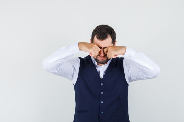 Jeune homme en chemise, gilet se frottant les yeux et à la triste