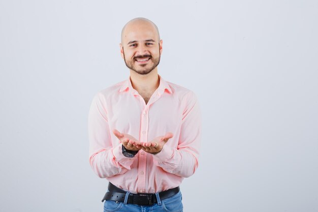 Jeune homme en chemise, jeans étirant les mains en coupe et semblant paisible, vue de face.