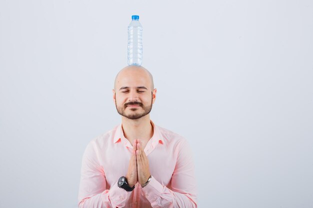 Jeune homme en chemise, jeans montrant le geste de namaste et semblant paisible, vue de face.