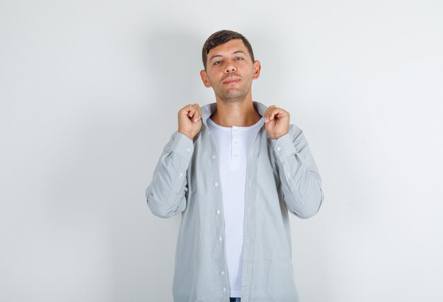 Jeune homme en chemise, jeans posant tout en maintenant le col et à la recherche de plaisir