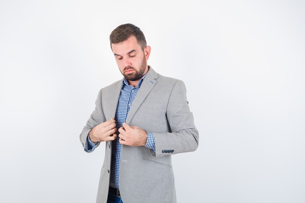 Jeune homme en chemise, jeans, veste de costume tenant des revers tout en posant et regardant sérieusement, vue de face.