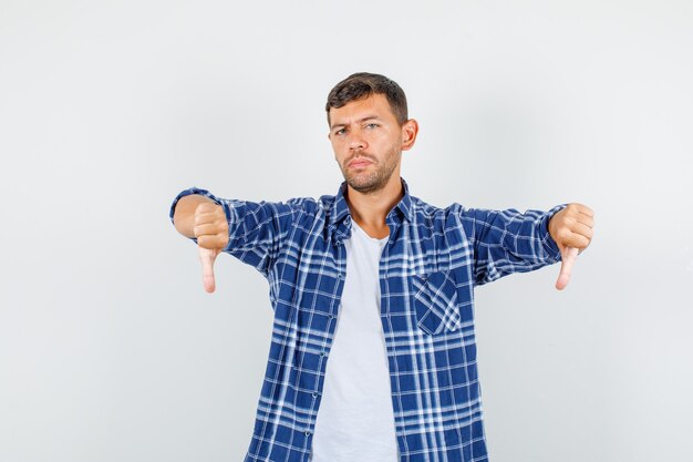 Jeune homme en chemise montrant les pouces vers le bas et à la déçu, vue de face.