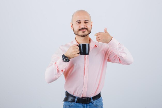 Jeune homme en chemise rose, jeans sentant l'odeur du thé, vue de face.