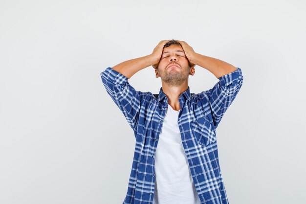 Jeune homme en chemise tenant la tête avec les mains et à la pitié, vue de face.