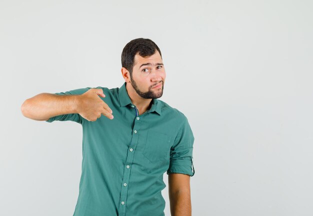 Jeune homme en chemise verte faisant un geste de pistolet, vue de face.