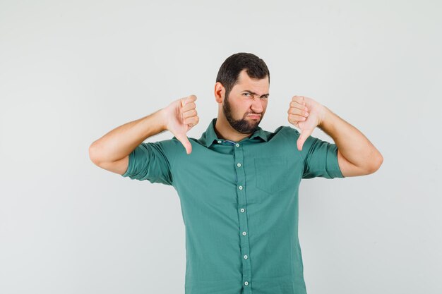 Jeune homme en chemise verte montrant le pouce vers le bas et l'air insatisfait, vue de face.