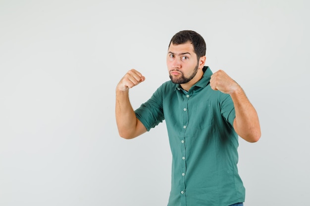 Jeune homme en chemise verte montrant ses poings et semblant agressif, vue de face.