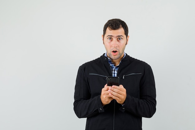 Jeune homme en chemise, veste à l'aide de téléphone portable et à la surprise