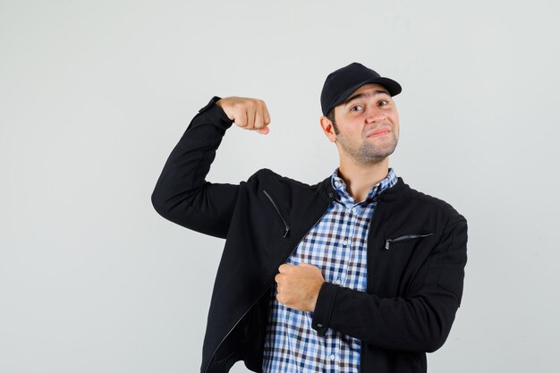 Jeune homme en chemise, veste, casquette montrant les muscles du bras et à la confiance