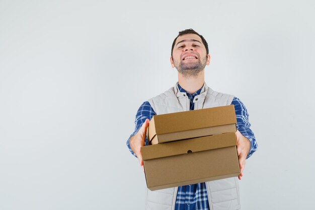 Jeune homme en chemise, veste donnant des boîtes à quelqu'un et à la vue de face, heureux.