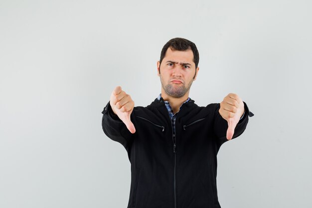 Jeune homme en chemise, veste montrant le double pouce vers le bas et à la sombre