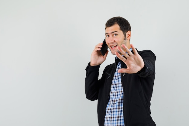 Jeune homme en chemise, veste parlant au téléphone mobile, faisant le geste d'attente et à la recherche positive