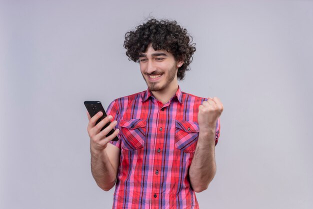 Jeune homme cheveux bouclés isolé chemise colorée smartphone oui poing