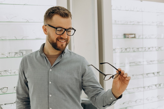 Jeune homme choisissant des lunettes au magasin d'optique