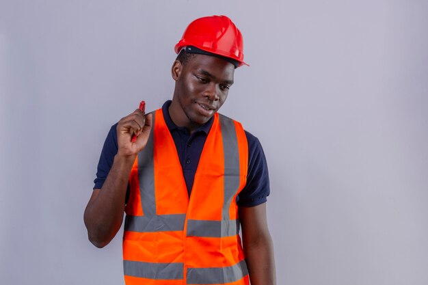 Jeune homme de constructeur afro-américain portant un gilet de construction et un casque de sécurité tenant une clé à molette à côté avec le sourire sur le visage debout