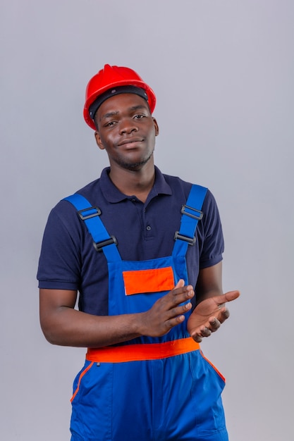 Photo gratuite jeune homme de constructeur afro-américain portant des uniformes de construction et un casque de sécurité applaudissant avec un sourire confiant sur le visage debout