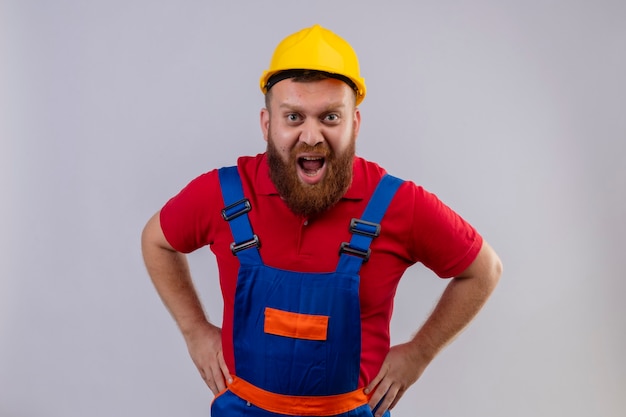 Jeune homme constructeur barbu en uniforme de construction et casque de sécurité criant avec une expression agressive