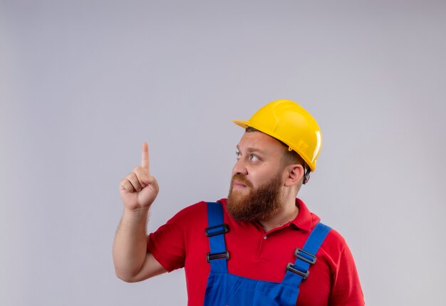 Jeune homme de constructeur barbu en uniforme de construction et casque de sécurité jusqu'à