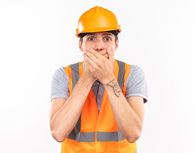 Jeune homme de constructeur effrayé dans la bouche couverte d'uniforme avec des mains