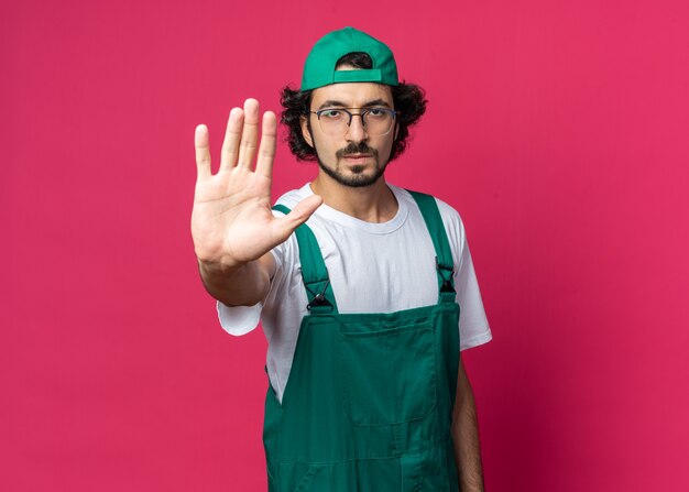 Jeune homme de constructeur strict portant l'uniforme avec la casquette montrant le geste d'arrêt