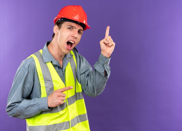 Jeune homme de construction impressionné en points uniformes sur le côté isolé sur un mur bleu avec espace de copie