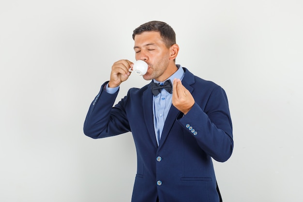 Jeune homme en costume de boire du café turc et montrant un signe savoureux et à la satisfaction