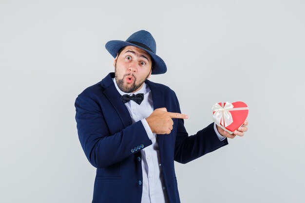 Jeune homme en costume, chapeau pointant sur la boîte actuelle et regardant étonné, vue de face.