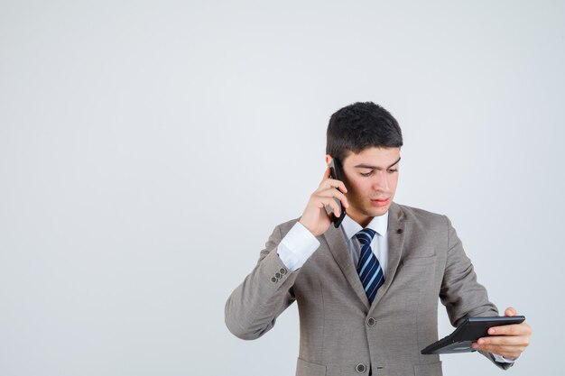 Jeune homme en costume formel parlant au téléphone, regardant la calculatrice