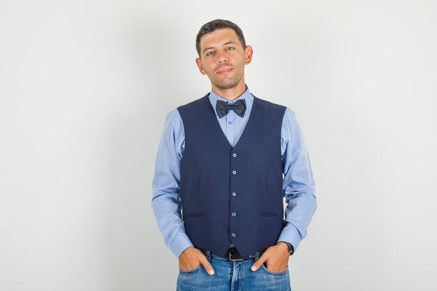 Jeune homme en costume, jeans debout avec les mains dans les poches et à la gaieté