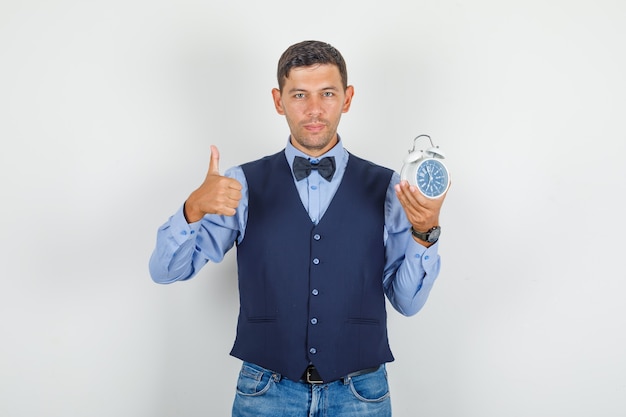 Jeune homme en costume, jeans montrant le pouce vers le haut avec réveil et à la satisfaction