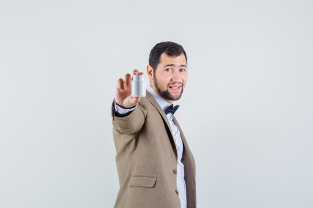 Jeune homme en costume montrant une bouteille de pilules et à la bonne humeur.