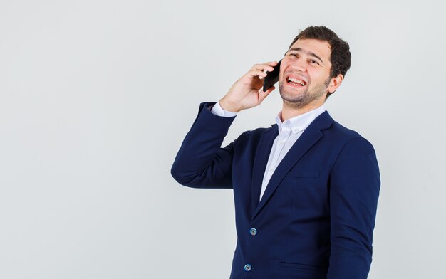 Jeune homme en costume de rire tout en parlant sur smartphone, vue de face.