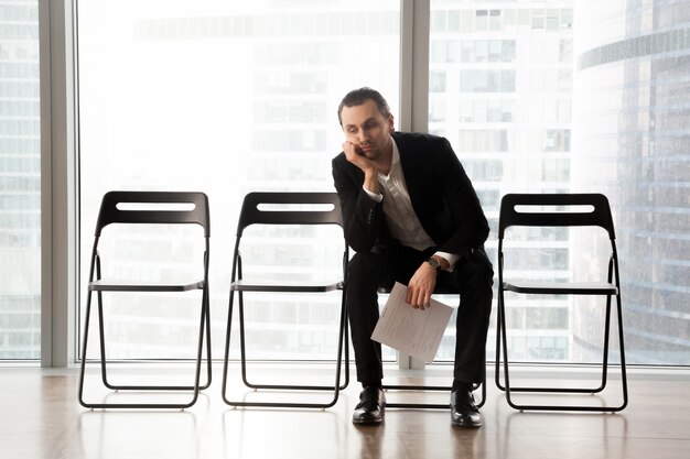 Jeune homme en costume s'ennuie assis dans la salle d'attente.