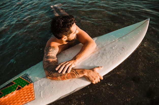 Jeune homme couché sur la planche de surf en mer